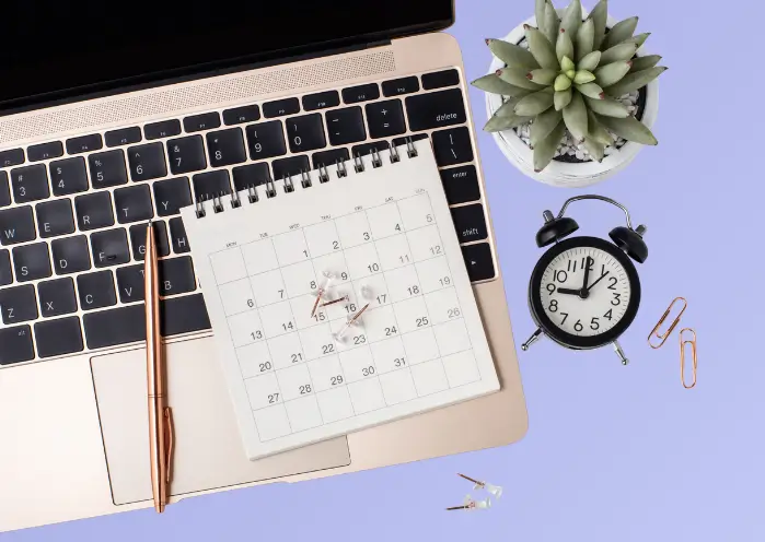 Espace de travail illustrant les outils utilisés pour le calcul horaire du travail : ordinateur, calendrier, horloge et accessoires de bureau.