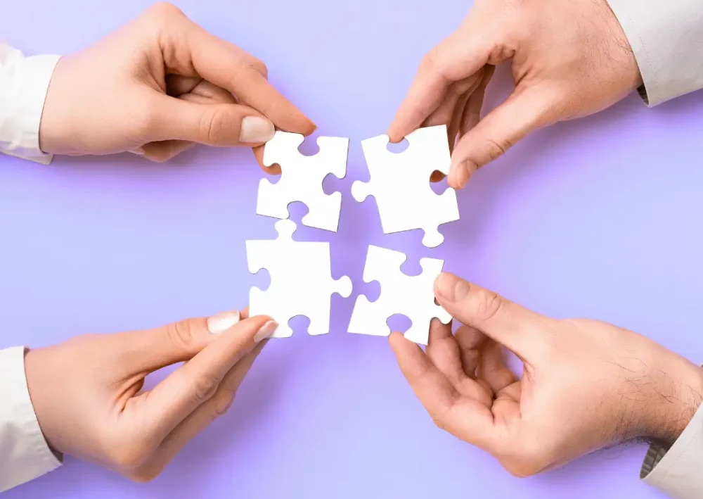 Mains assemblant des pièces de puzzle – symbole de collaboration et d’organisation du travail en équipe.